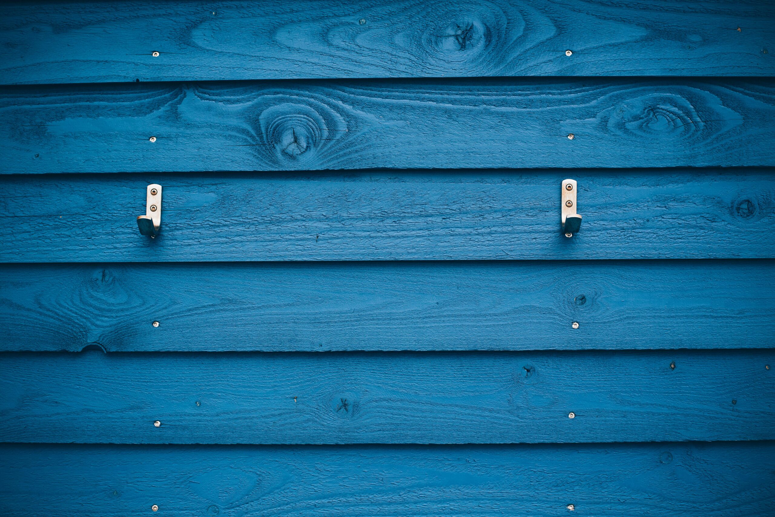 A vibrant blue wooden wall with two metal hooks creates a striking visual pattern.